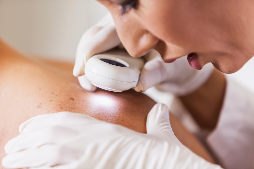 A woman scans a man's shoulder with a small handheld magnifying glass and torch