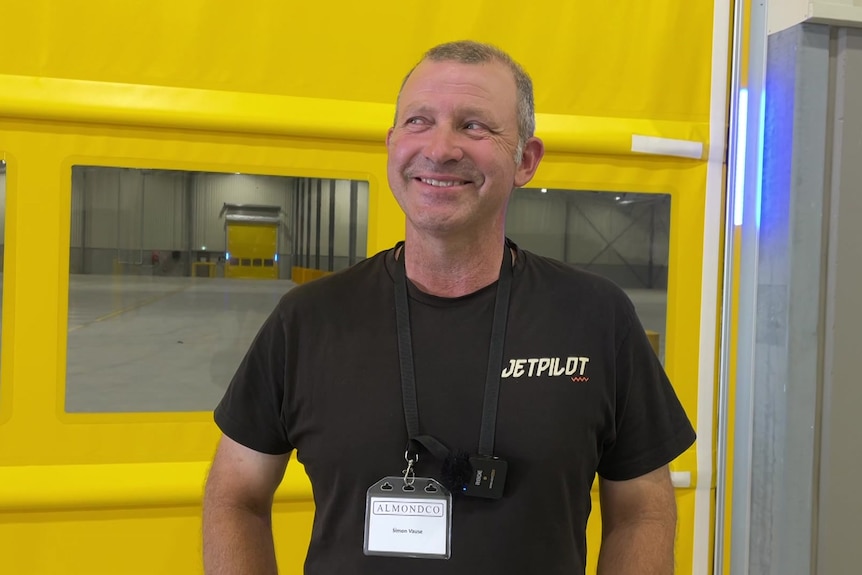 A man in a dark t-shirt stands in front of a a yellow fabric divider with a cheeky smile
