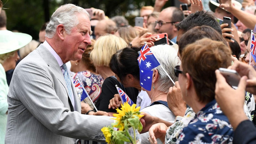Prince Charles greets a crowd of people waving Australian flags and holding up mobile phones
