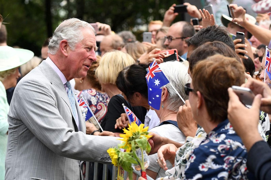 Prince Charles greets a crowd of people waving Australian flags and holding up mobile phones
