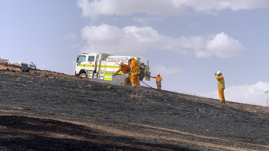 Firefighters hosing black soil in front of a fire truck