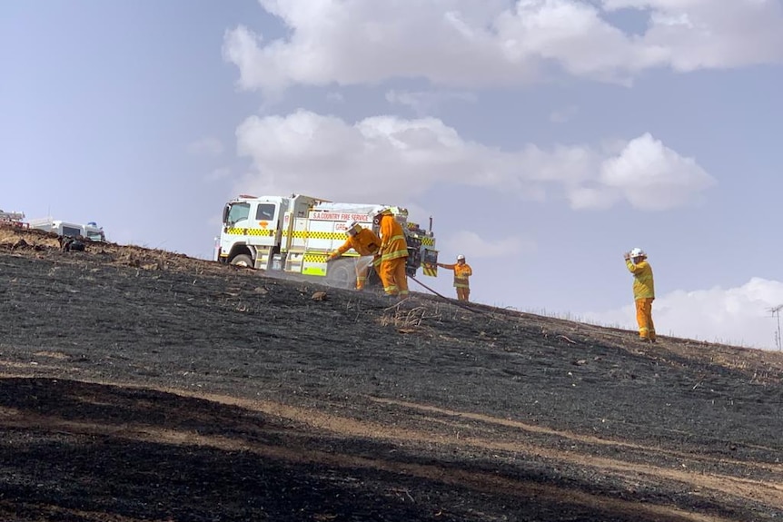 Firefighters hosing black soil in front of a fire truck