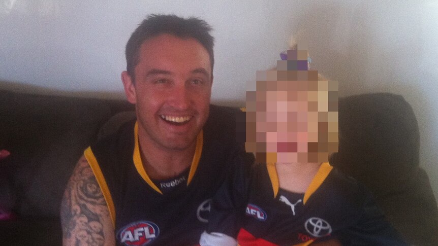 A man holding a girl on a sofa, both wearing Adelaide Crows jumpers