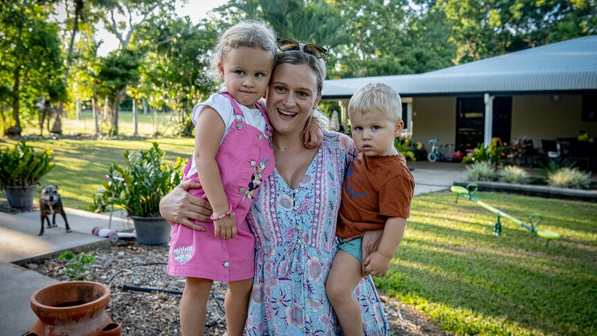 A woman holding two children in a backyard