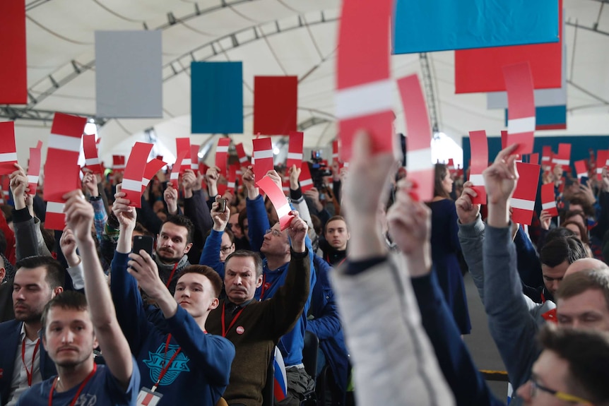 A crowd of people hold up red and white sheets of paper to vote.