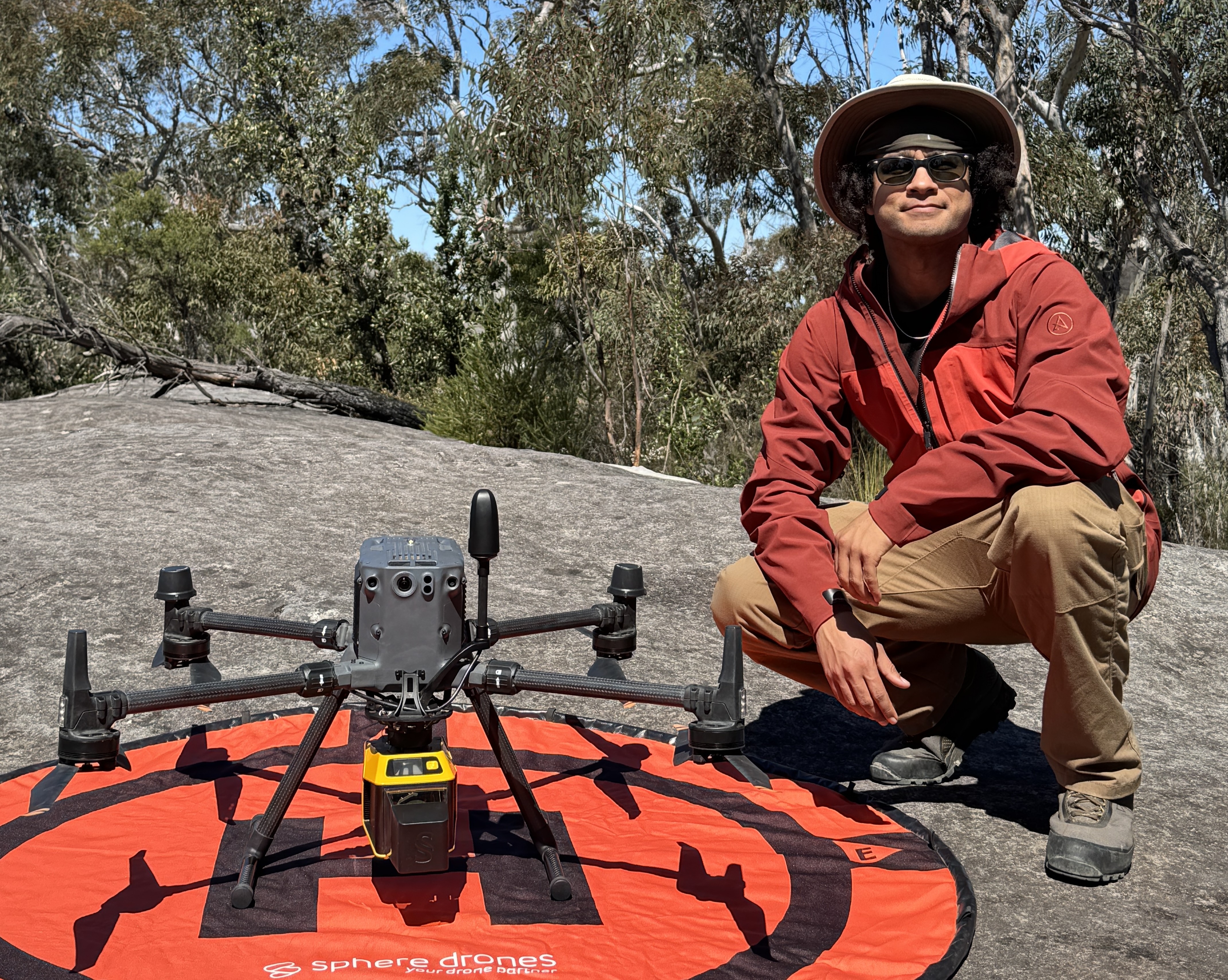 A man sitting next to a drone on a rock