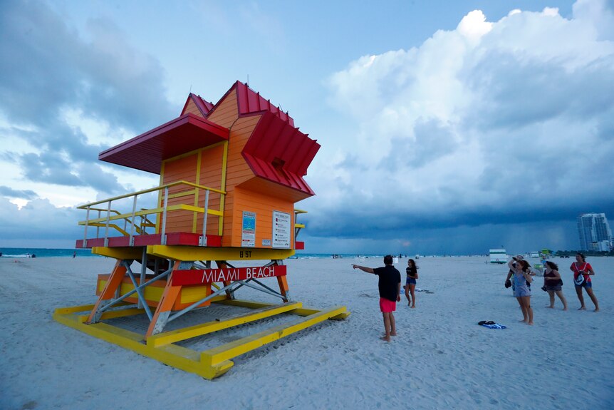 Beach goers point at a Miami Beach lifeguard stand as storms from a hurricane system brood in the background