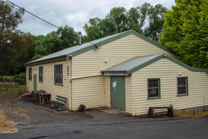 A cream coloured weatherboard building in front of trees