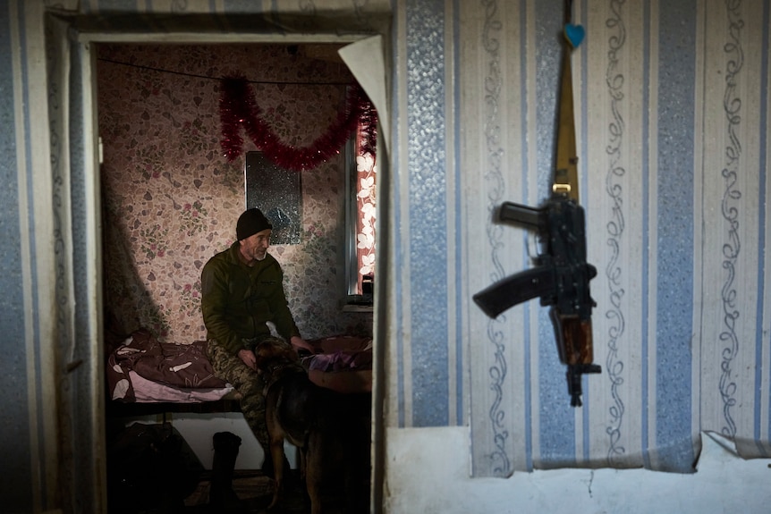 A Ukrainian soldier pets a dog as he rests inside a house.