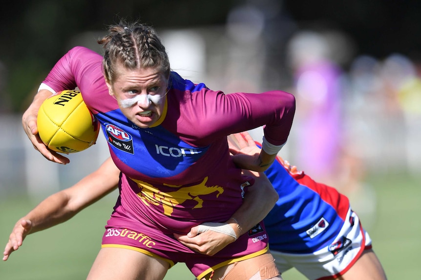 Nat Exon holds the ball under her right arm as she is tackled by a Melbourne Demons AFLW player.