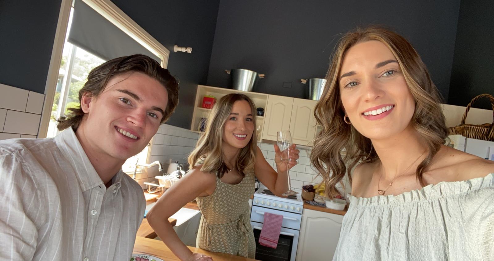 A selfie photo taken in a kitchen showing a young man and two young women. All are smiling.