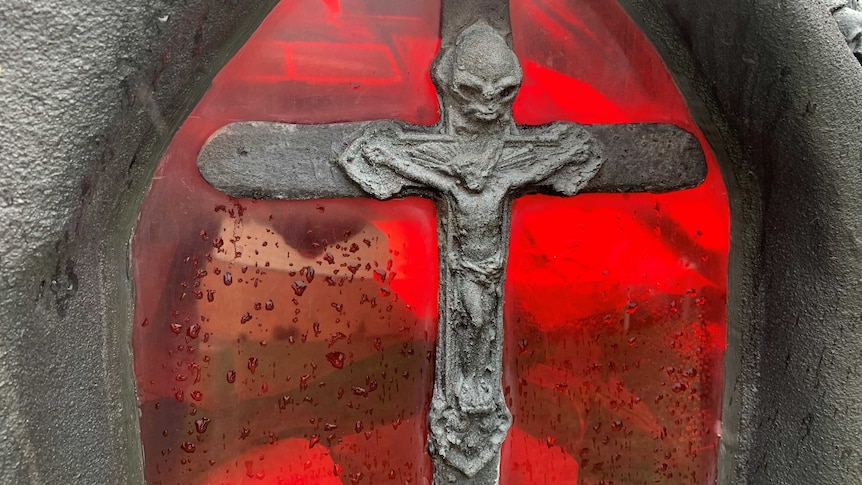 Picture of red stained glass window on hears with silver cross.