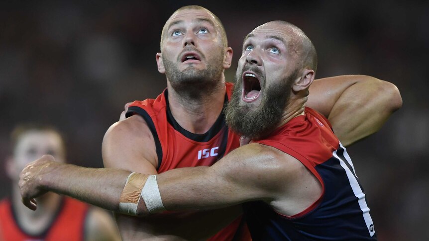 Tom Belchambers and Max Gawn push against each other as they look at the ball in the air.