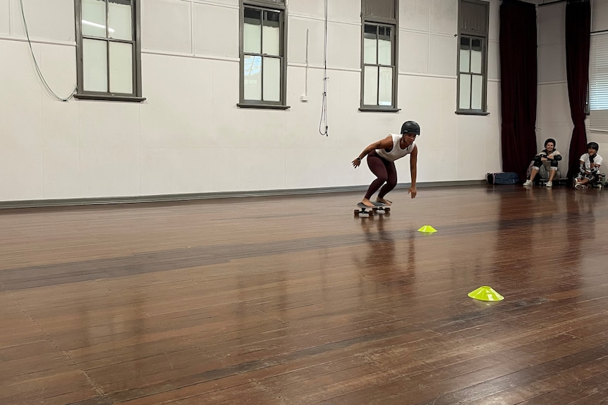 A woman skateboarding in a hall with a wooden floor.