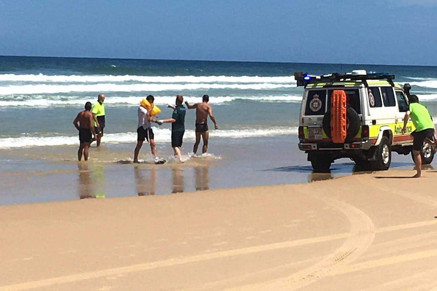 A group of people standing in water at the beach near an ambulance