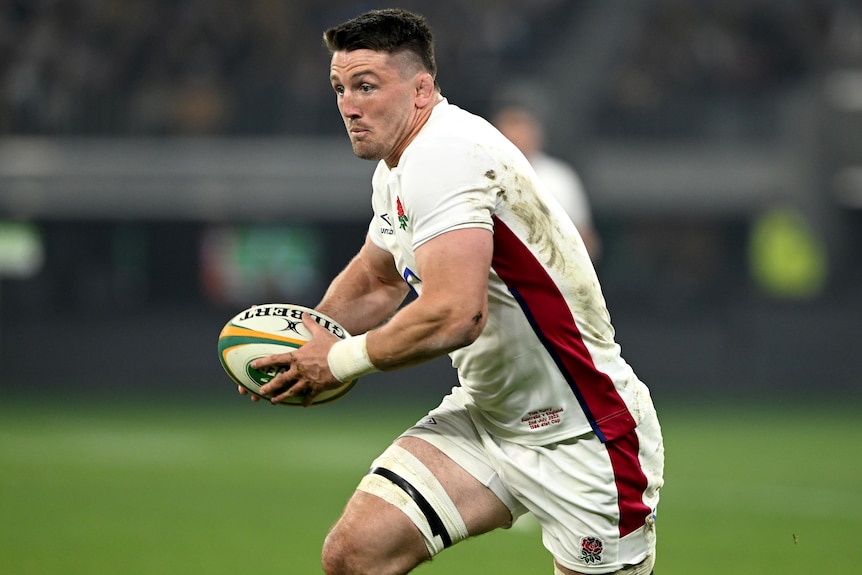 A male England Test rugby player holds the ball as he makes a run against Australia.