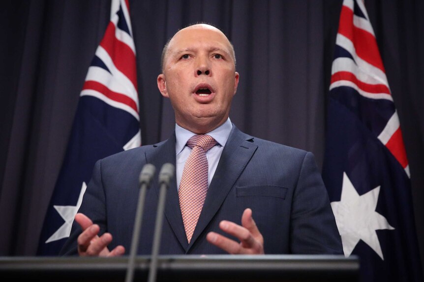 Mr Dutton is standing in front of two Australian flags and a blue curtain, mid sentence. He's standing behind a lectern.