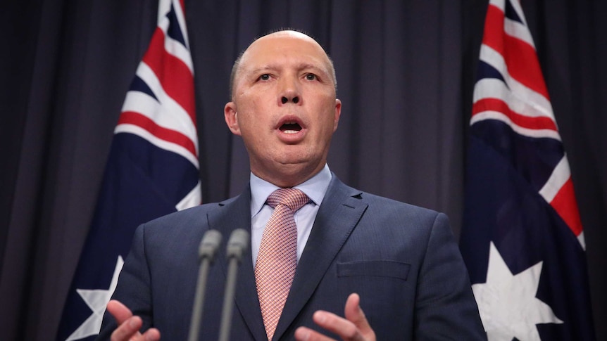 Mr Dutton is standing in front of two Australian flags and a blue curtain, mid sentence. He's standing behind a lectern.