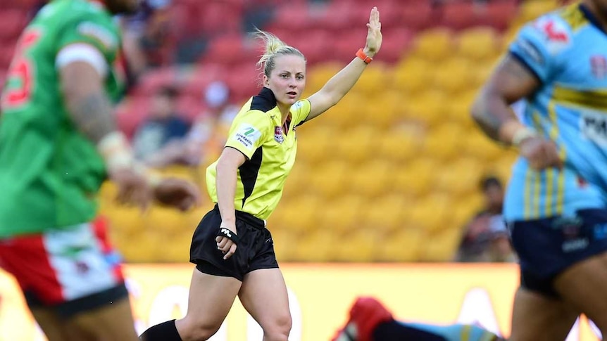 A female rugby league referee runs and raises her left arm as she officiates a match.
