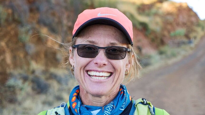 A smiling woman stands outside on a red dirt road in exercise gear.