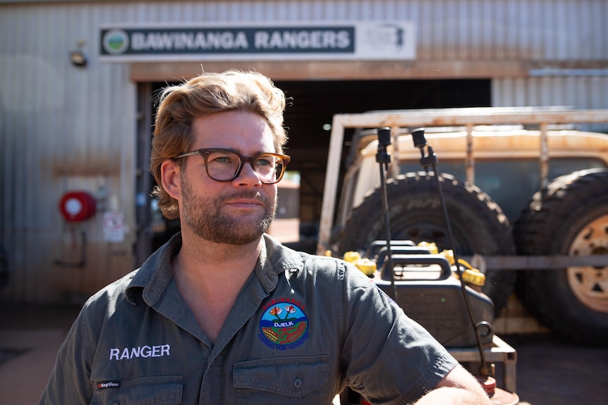 Ranger manager Tom Nagle leans on the back of a ute, a large shed is behind him. 