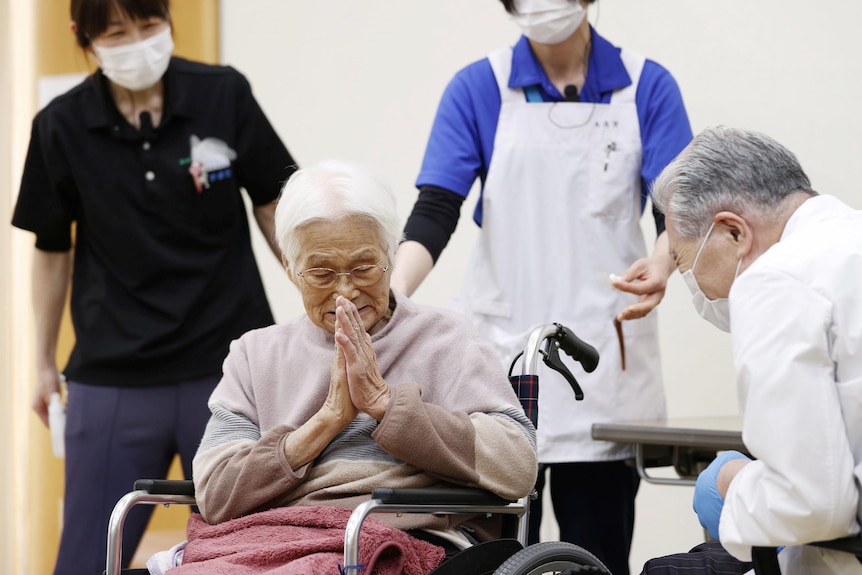 A Japanese woman in a wheelchair bows with clasped hands to a doctor 