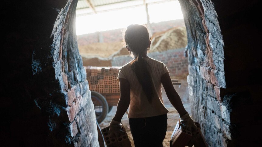 A 10-year-old girl carries bricks out of a kiln in Cambodia.