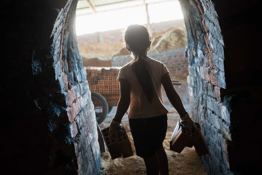 A 10-year-old girl carries bricks out of a kiln in Cambodia.