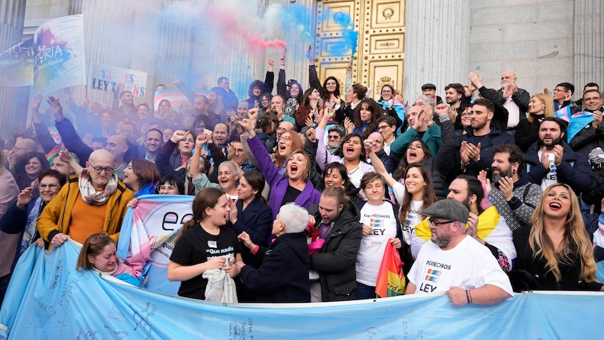 A group of people celebrating with blue pink and white smoke bombs