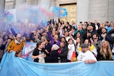 A group of people celebrating with blue pink and white smoke bombs