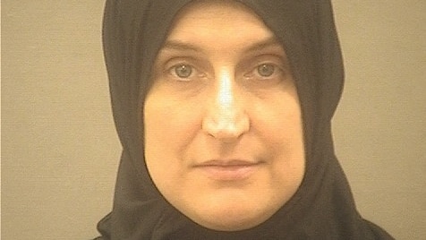 A middle aged woman in a dark headscarf looks into the camera as she poses for a mugshot.