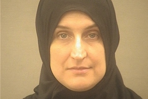 A middle aged woman in a dark headscarf looks into the camera as she poses for a mugshot.