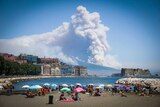 Smoke rises from wild fires burning on the slopes of Mt Vesuvius volcano as people sun bathe on a beach.