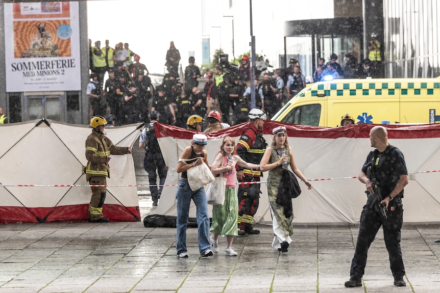 Three young women walk through a police barricade. On the other size is a large group of police