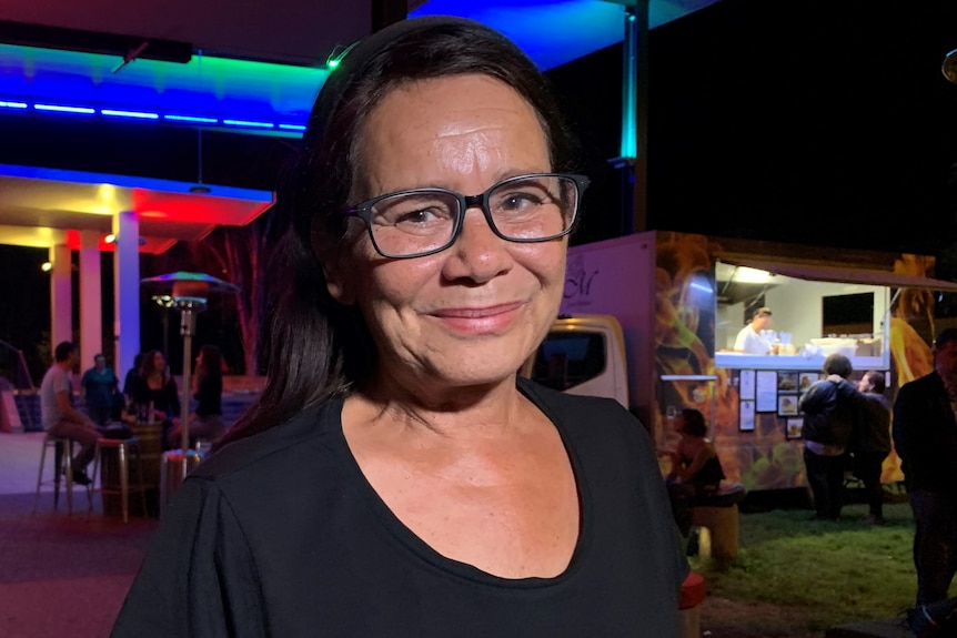 Woman wearing black shirt with glasses standing outside a food truck at night.