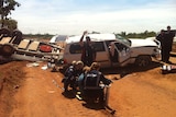 A crashed car and boat on a remote dirt road, with paramedics responding.