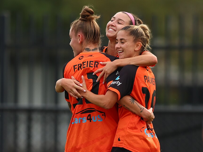 Three soccer players wearing orange and black hug each other during a match