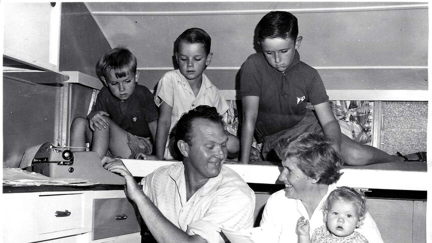 An old black and white photograph of a woman looking at some papers while surrounded by a man and children.