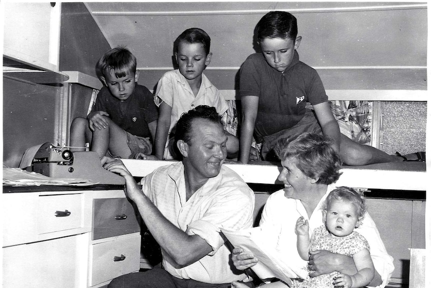 An old black and white photograph of a woman looking at some papers while surrounded by a man and children.
