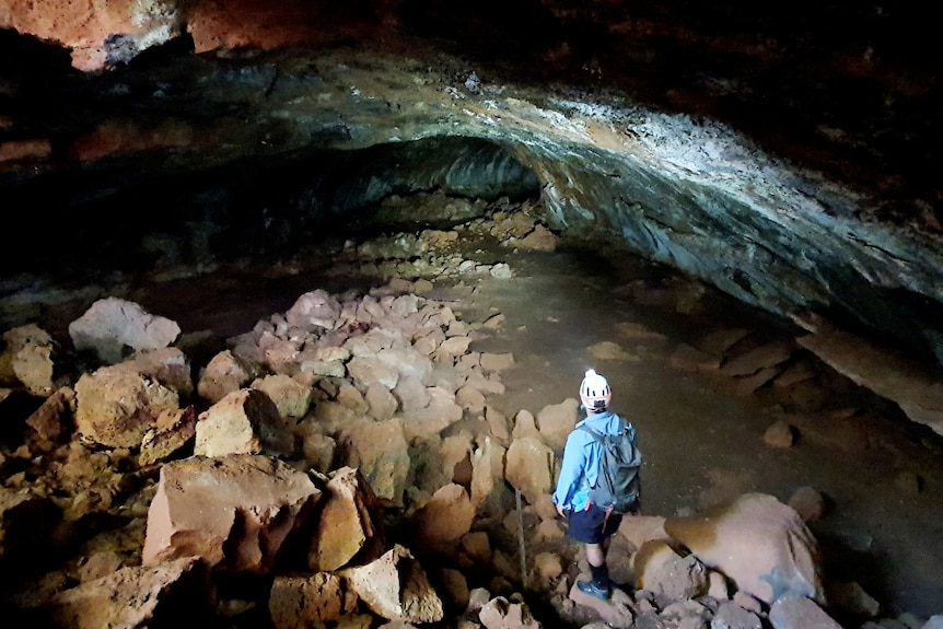 A person stands in a cave with a torch.