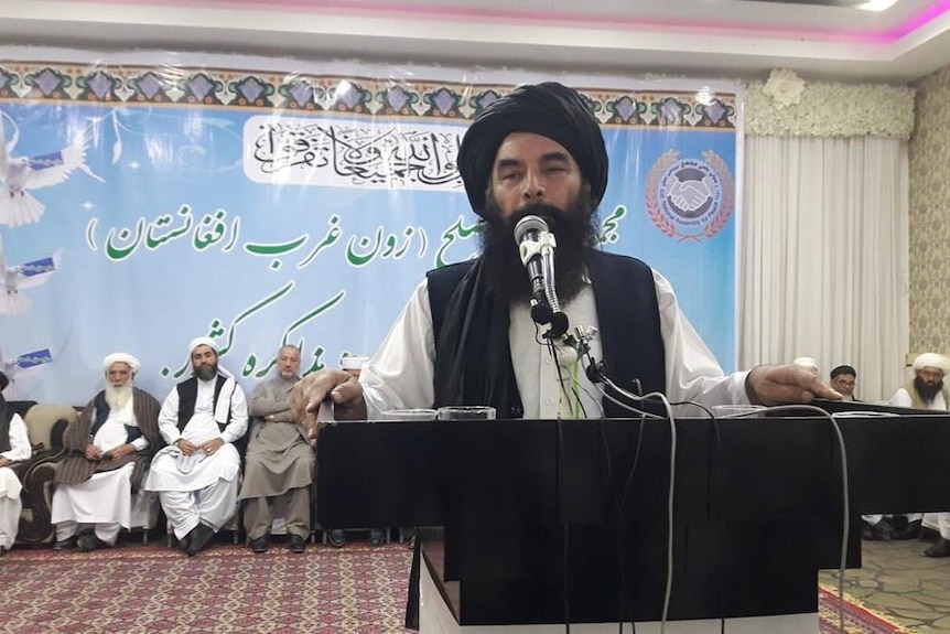A man wearing traditional Afghan dress and headwear speaks from a podium.