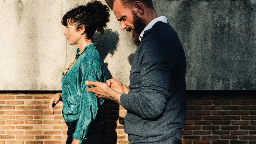 A couple walking through a street with the man looking at his phone