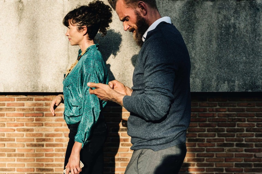 A couple walking through a street with the man looking at his phone