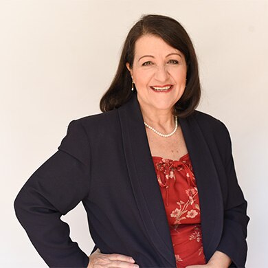 A lady standing in a suit with brown hair smiling at the camera 