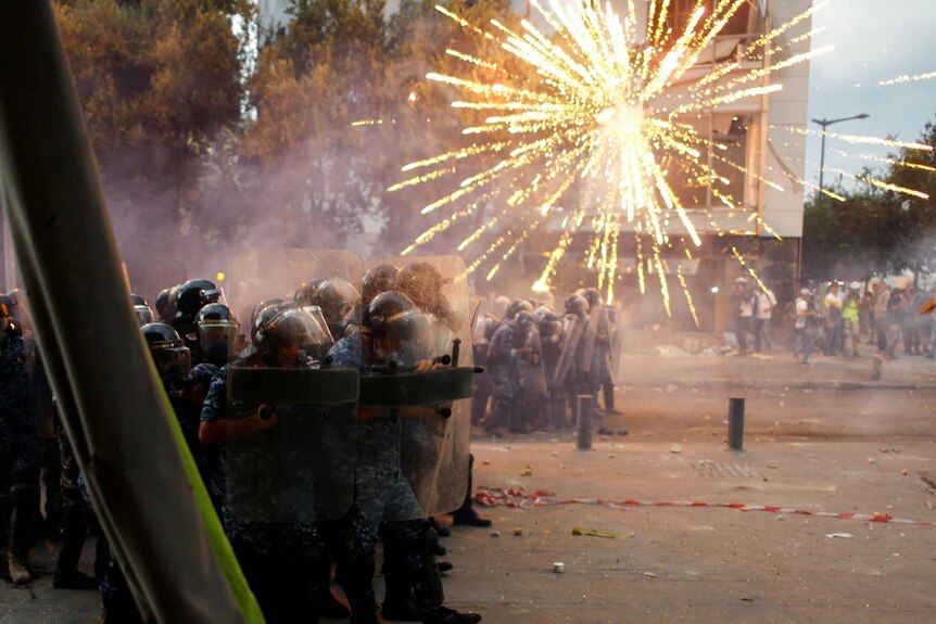 A firework explodes as police in riot gear stand in a street