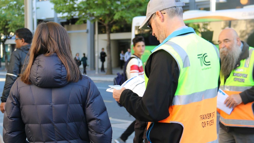 A volunteer helps a woman find which bus she needs to catch to work, as Canberra's new bus timetables come into place.