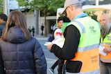 A volunteer helps a woman find which bus she needs to catch to work, as Canberra's new bus timetables come into place.