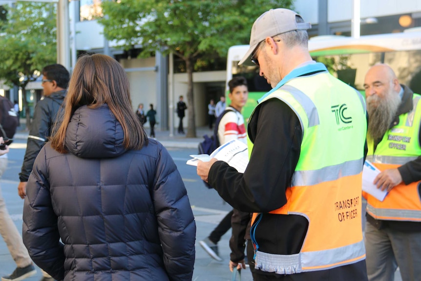 A volunteer helps a woman find which bus she needs to catch to work, as Canberra's new bus timetables come into place.