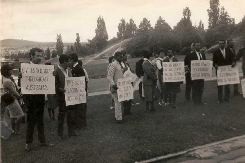 Black and white photograph of people rallying on a lawn carrying signs calling for equal rights for Aboriginal people.