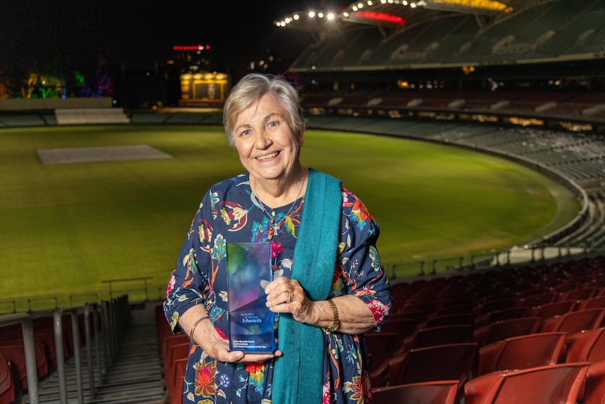 A woman with a teal scarf draped over her shoulder and colourful top smiling as she holds on to an award